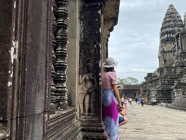 Femme au chapeau regardant des sculptures anciennes en pierre d'un temple
