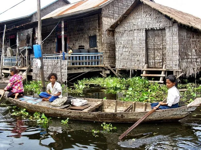Des habitants dans de petits bateaux en bois devant des maisons traditionnelles sur pilotis