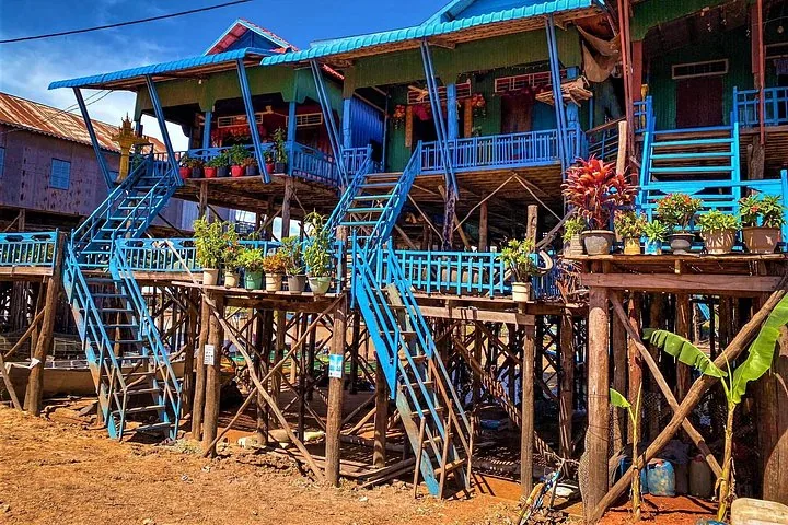 Maisons sur pilotis peintes en bleu et vert vif pendant la saison sèche, avec la terre à découvert.