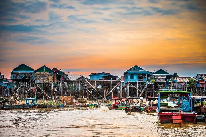 Colorful stilted houses and small boats in Kampong Phluk during sunset.