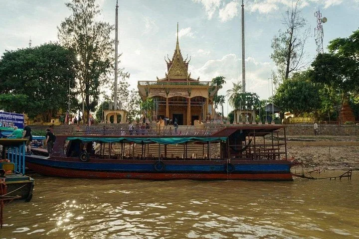 Un grand bateau de passagers amarré près d’un temple cambodgien au bord de la rivière.
