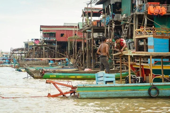 Local men working on a wooden boat alongside stilted houses at Kampong Phluk.